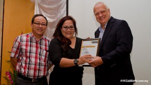Mary Pudun receiving her award from Professor Mienczakowski while Chief Operating Officer Nicholas Ching looks on.